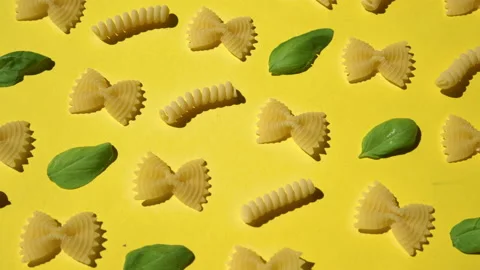 Uncooked curly pasta and basil leaf pattern on yellow background. Traditional Stock Footage 137109144