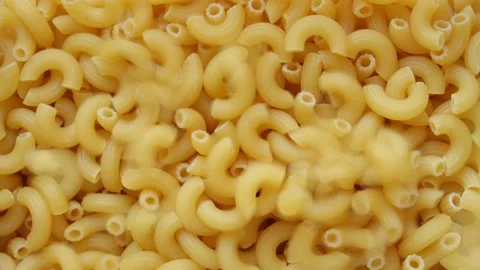 Uncooked elbow macaroni being poured into a heap of pasta full screen Stock Footage 193993485
