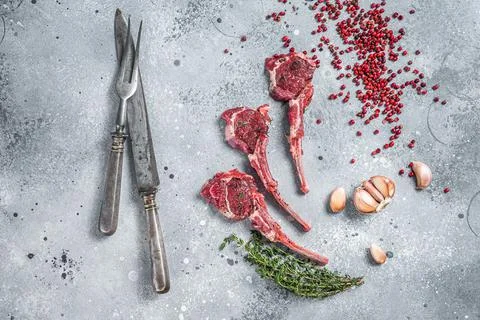 Uncooked lamb meat chops steaks on a butcher table with pepper and thyme. Gray Stock Photos