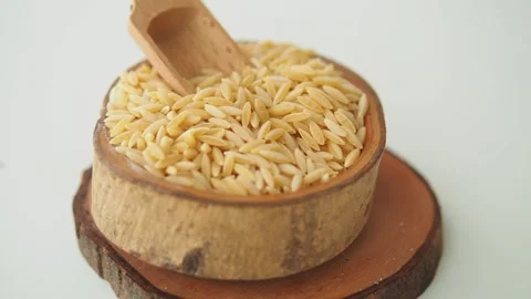 Uncooked orzo pasta grains in rustic wooden bowl on white background motion.. Vídeos de archivo 332202317