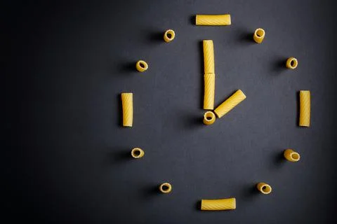 Uncooked pasta designed in clock shape on dark background. Stock Photos
