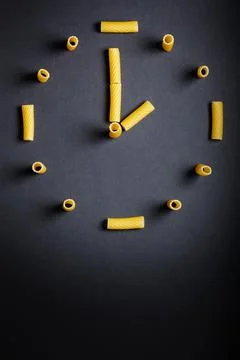 Uncooked pasta designed in clock shape on dark background. vertical photo Stock Photos