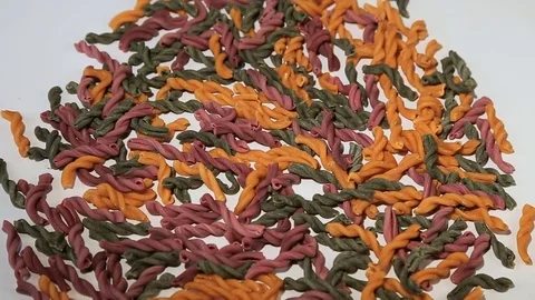 Uncooked pasta in the form of spiral of different colors rotates on white Stock Footage 75575472