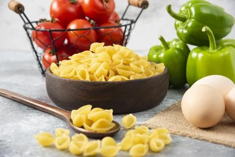 Uncooked pasta in shell shaped with raw chicken eggs placed on stone table Foto stock