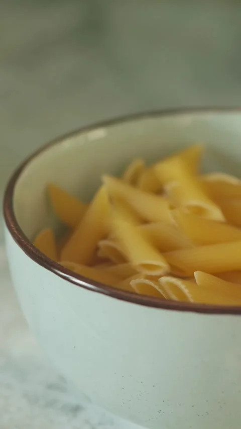 Uncooked Penne Pasta Falling into Ceramic Bowl Close-Up Stock Footage 316150665