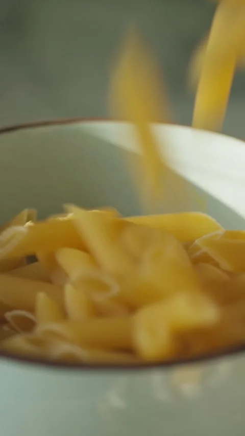 Uncooked Penne Pasta Falling into Ceramic Bowl Close-Up Stock Footage 316150679