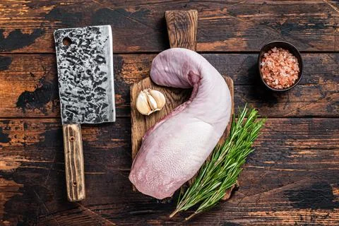 Uncooked Raw beef or veal tongue on butcher board with meat cleaver. Dark wooden Stock Photos