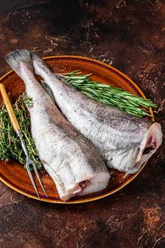 Uncooked Raw cod or codfish fish in rustic plate with herbs and fork. Dark Stock Photos