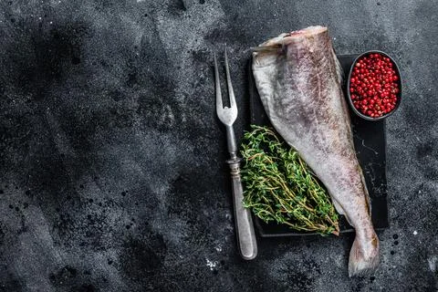 Uncooked Raw cod whole fish on marble board with thyme. Black background. Top Stock Photos