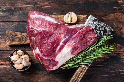 Uncooked Raw mutton lamb thigh on butcher board with meat cleaver. Dark wooden Stock Photos