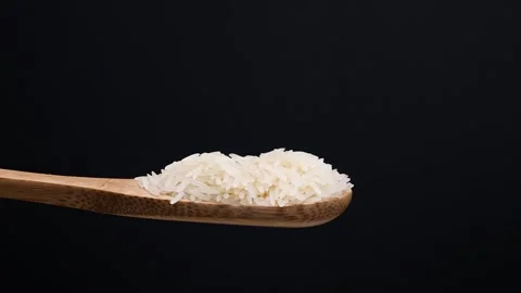 Uncooked raw white long grain rice pour drop fall on wooden spoon spin rota.. Stock Footage 261982996