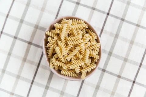 Uncooked spiral pasta in the ceramic plate. plaid tablecloth background. to.. Stock Photos