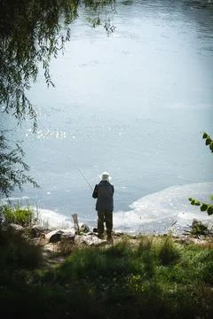 Undefined man is fishing in the Dniester River. Dirty film of sewage near the Stock Photos