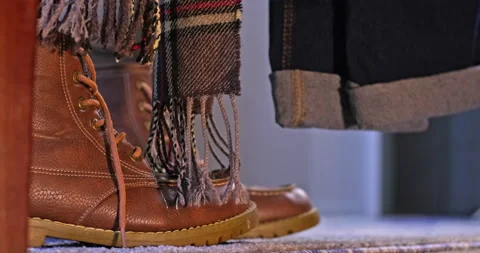 Under the bed view of fall boots with a scarf and blue jeans hanging from bed Stock Footage 204046852
