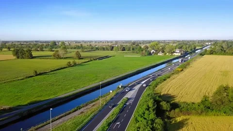 Under blue sky, continuous busy car flow on a highway by a small river. Drone Vídeos de archivo 153479316