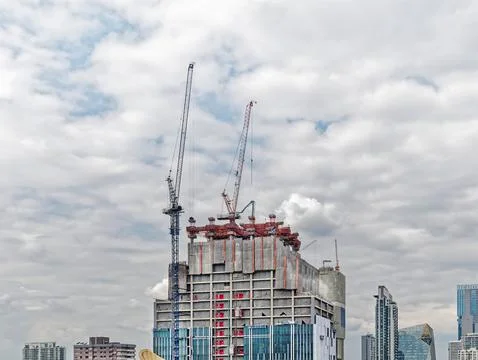 Under Construction Building with Cranes and Workers Against Cloudy Sky Stock Photos