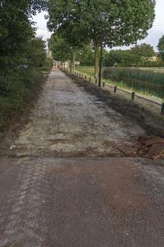 Under-construction walkway with removed asphalt along a canal and trees Foto stock