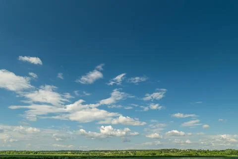 Under a deep blue sky adorned with fluffy white clouds, a lush green horizon  Stock Photos