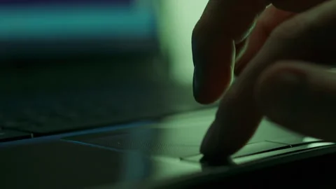 Under dim lighting, a hacker programmer is intently busy at his laptop, usin Stock Footage 255289689