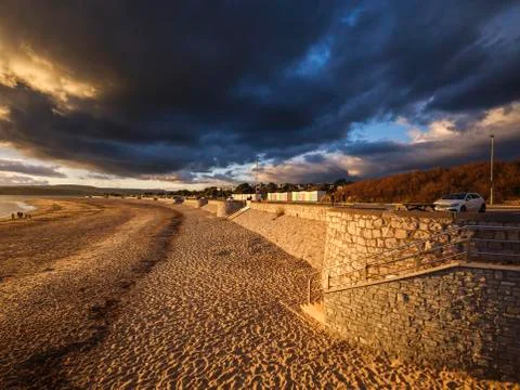 Under dramatic clouds, strong warm sunlight illuminates the beach and sea Foto stock