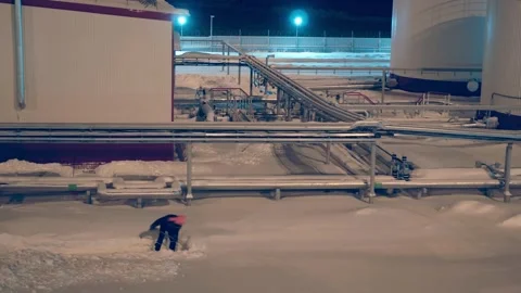 Under glow of industrial lights, worker clears snow at factory during night Stock Footage 281094310