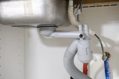 Under kitchen sink showcasing complex gray PVC drain pipes, corrugated hose.. Foto stock