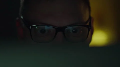 Under the light of a laptop computer screen, a programmer wearing glasses wo Stock Footage 263920814