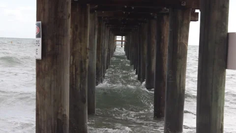 Under Pier View with Waves Crashing on Wooden Pilings Stock Footage 334700413