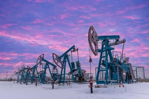 Under the purple-blue sky with clouds seven Oil pumpjack winter working. Oil  Stock Photos