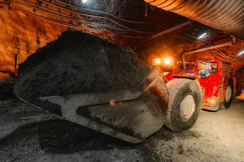 An underground loading machine carries a full bucket of ore. Special low-profile Stock Photos