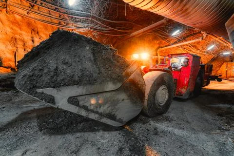 An underground loading machine carries a full bucket of ore. Special low-profile Stock Photos