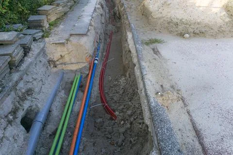 Underground utility trench with red optical fiber cables installed in dirt Foto stock