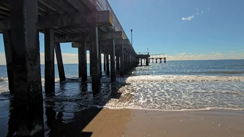 Underneath the Pier, A scenic view of ocean waves and sandy beach seen from Stock Footage 299913763