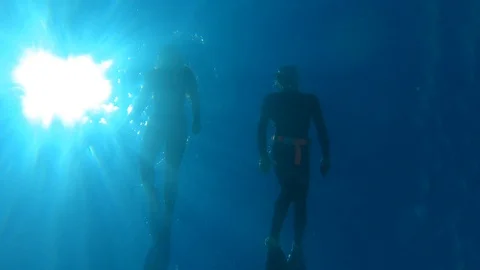 Underneath view of two people snorkeling on surface in blue water on a sunny day Stock Footage 124457858
