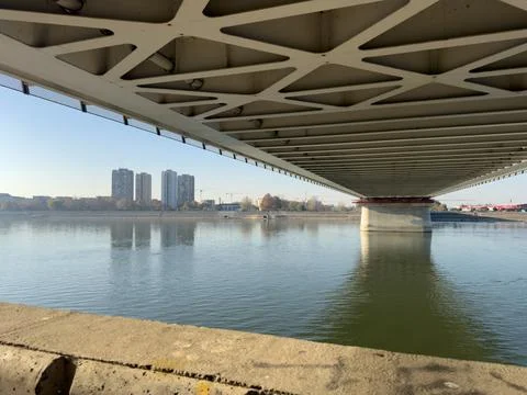 Underside of concrete bridge over calm river with distant cityscape Stockfoto's