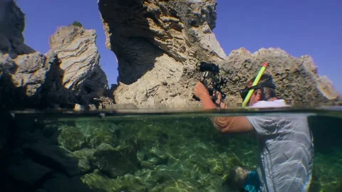 Underwater cameraman raises a camera above the water to capture a coastal rock Vídeo Stock 237445353
