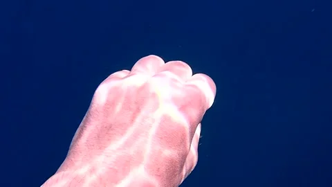 Underwater human hand making grabbing gestures with light ripple patterns Stock Footage 343007302