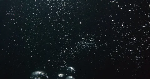 Underwater oxygen bubbles rise to the surface of a dark abyss in slow motion Stock Footage