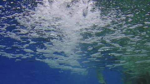 Underwater view looking up at the bright blue water surface. White bubbles .. 库存影片 341783333