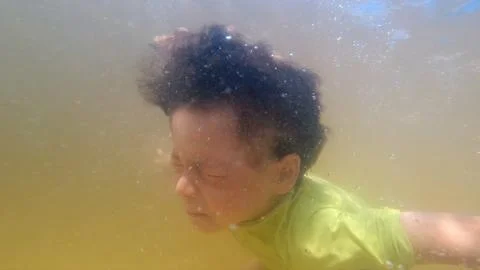 Underwater view of young boy diving into a murky thermal pool water Stock Photos