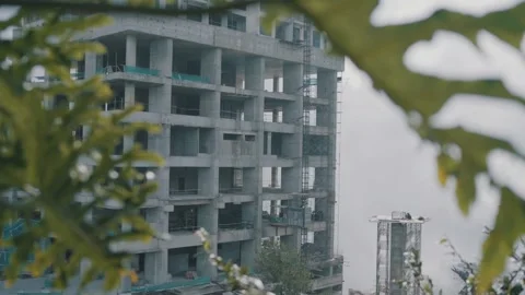 Unfinished concrete building under construction, framed by blurred foliage in Stock Footage 295975166