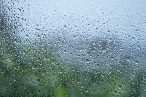 Unfocus background rain drops on window with green tree and blue sky. Stock Photos