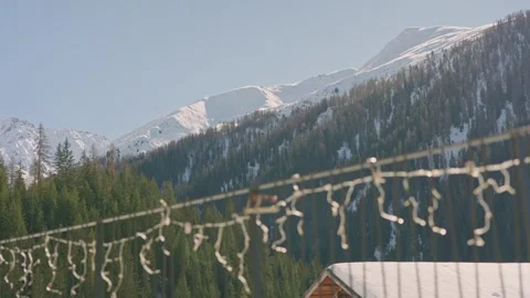 Unfocused festive lights hanging in front of a beautiful snowy mountain 스톡 동영상 334649129