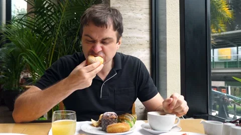 Unhappy angry young man eats fresh baked goods and does not enjoy his food Stock Footage 165547534
