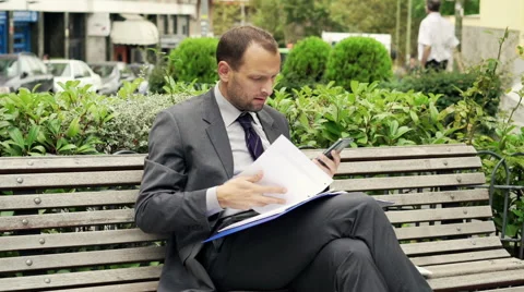 Unhappy businessman comparing data on smartphone and documents on bench HD Stock Footage 43337601