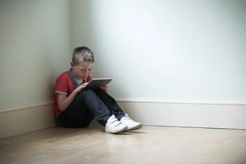 Unhappy Child Sitting In Room With Digital Tablet Foto stock