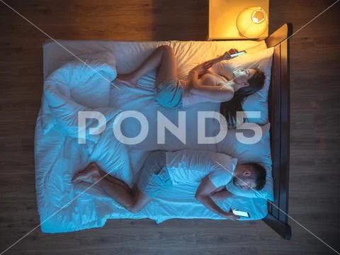 The unhappy couple with smartphone lay on the bed. night time. view from abov Stock Photos