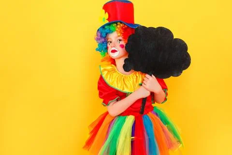 Unhappy girl in clown costume and hat holding black table Stock Photos
