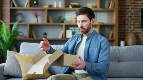 Unhappy man received a parcel with wrong product sitting on sofa in living room  Stock Footage 279083916