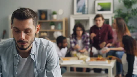 Unhappy man sitting alone while young people celebrating holiday in background Stock Footage 106389845